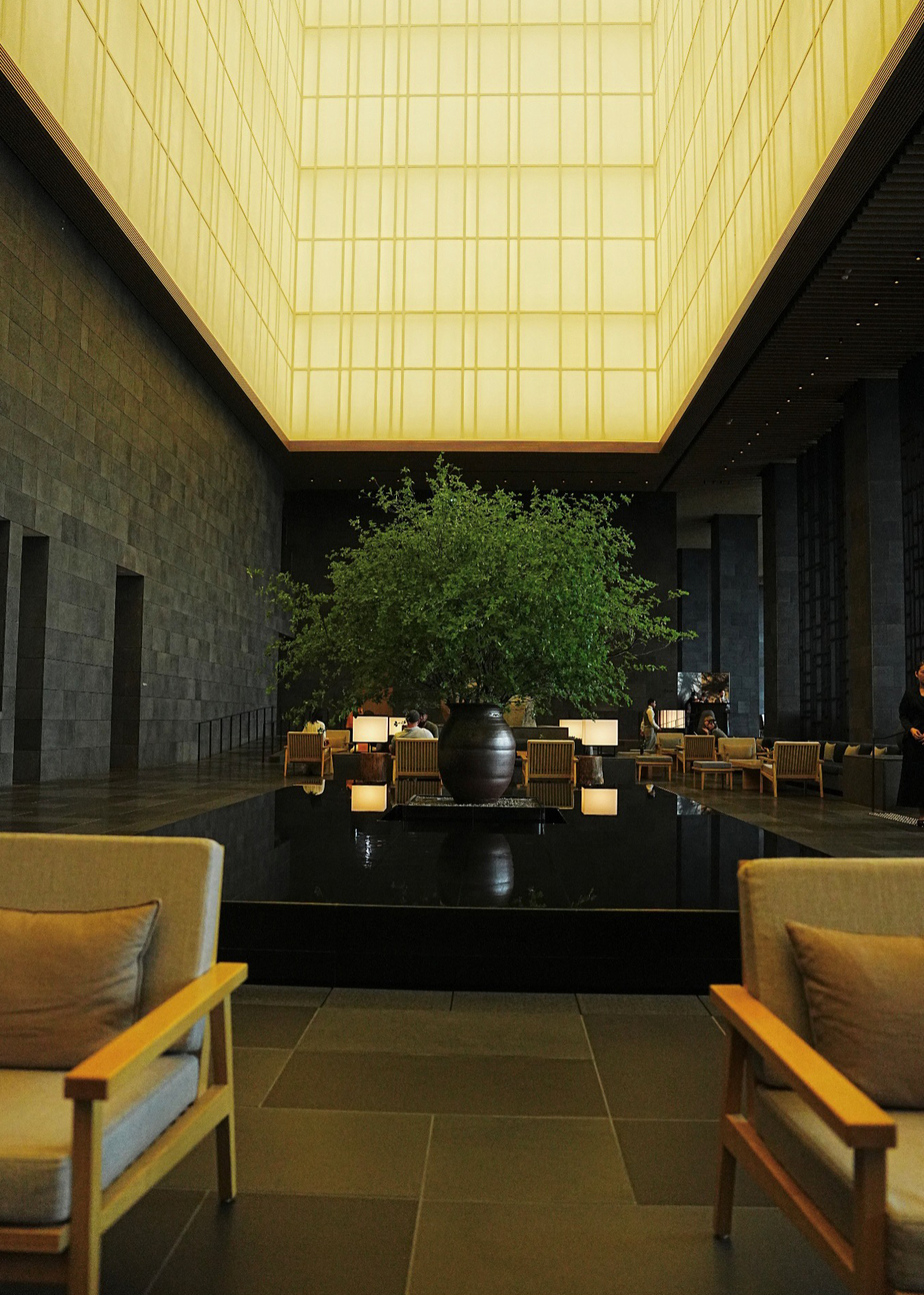 Double-height lobby atrium with a backlit ceiling, reflecting pool and stone walls